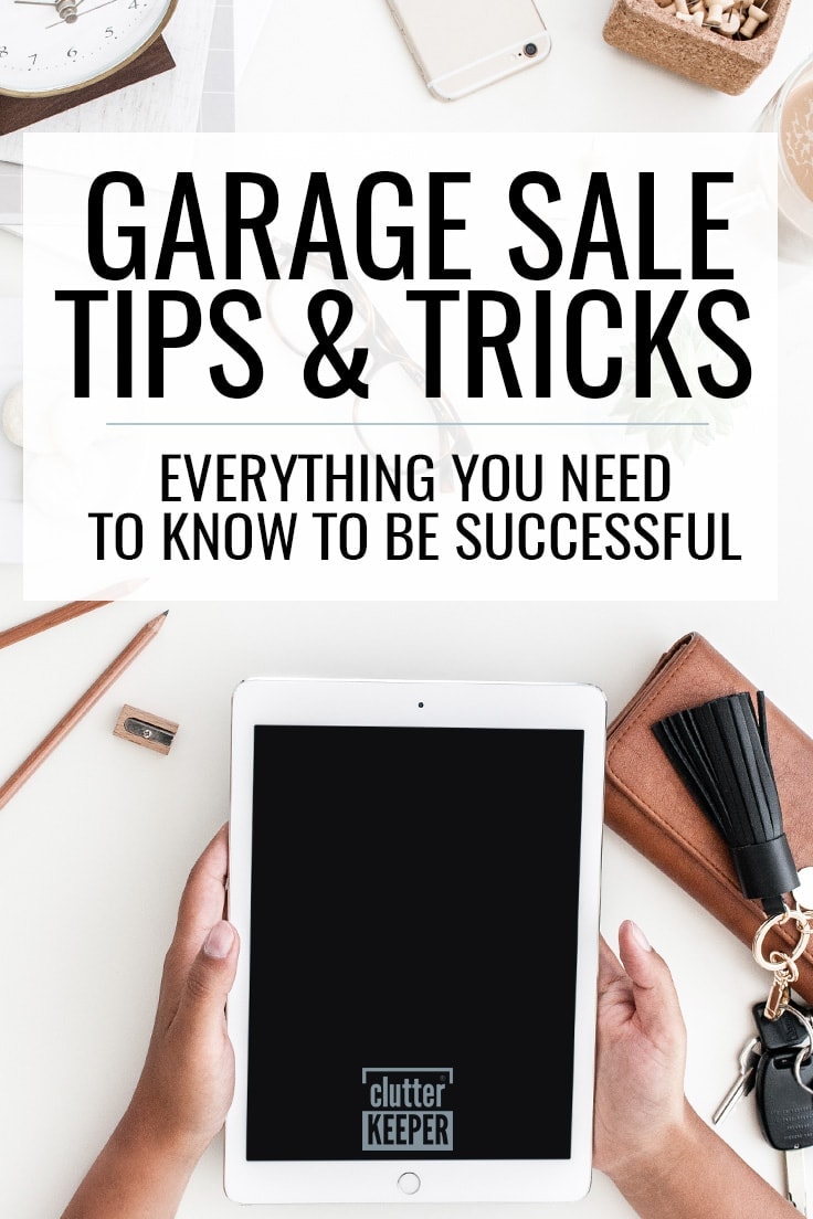 Garage Sale Tips & Tricks - Everything You Need to Know to Be Successful. An overhead shot showing two hands holding an iPad. Nearby are pencils, a sharpener, a clock, eyeglasses, a wallet and keys as someone prepares to host a yard sale.