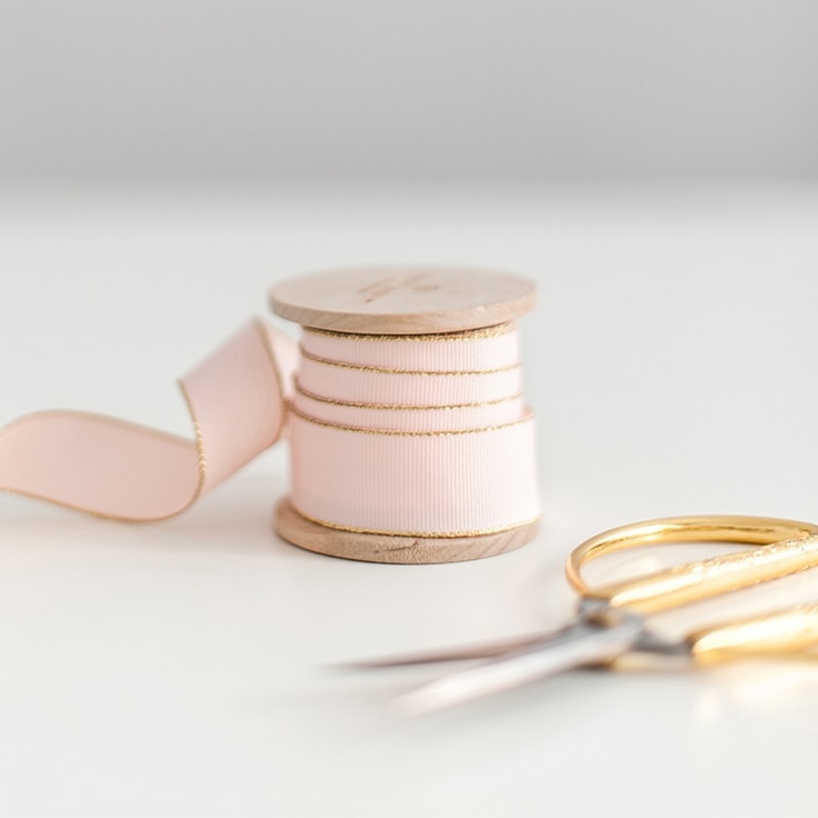 The image shows a spool or ribbon and a pair of scissors with gold handles to illustrate your complete guide to sewing room organization.